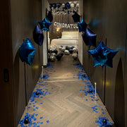 Decorated hallway with blue balloons and confetti leading to a bedroom with 'Congratulations' banner.