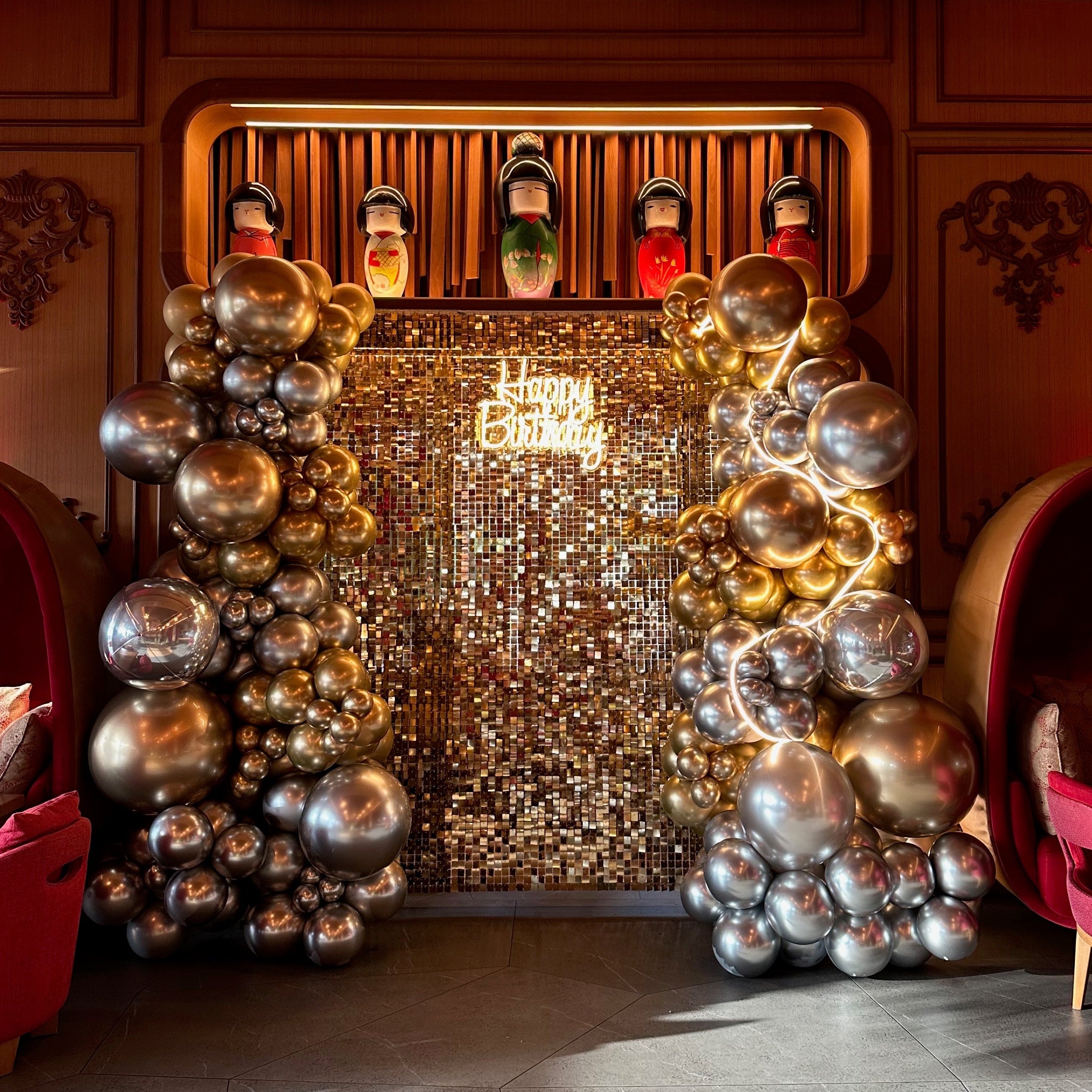 Decorative setup with balloons and a backdrop featuring a logo in a room with red chairs.