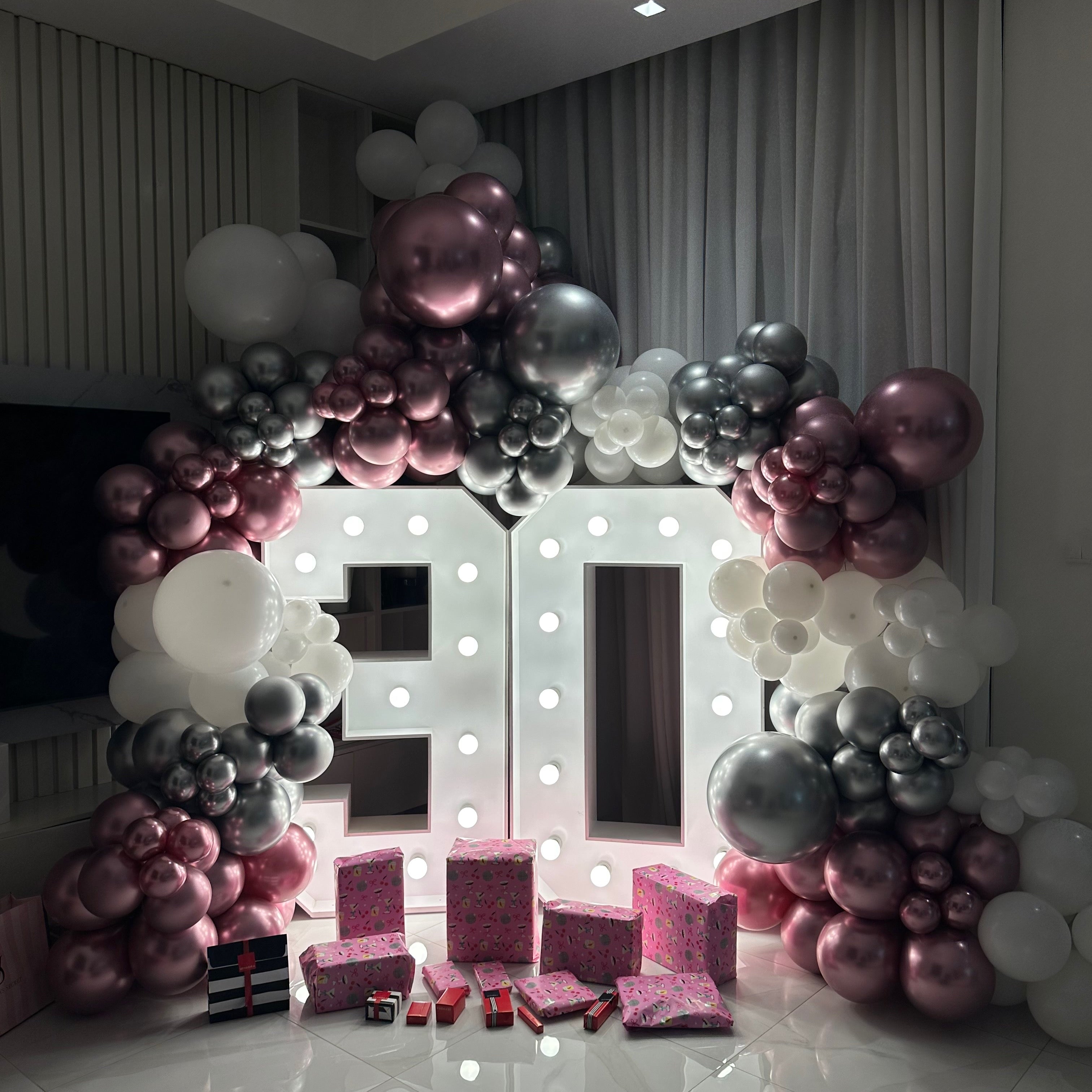 Decorative balloon arch with pink, silver, and white balloons in a room.